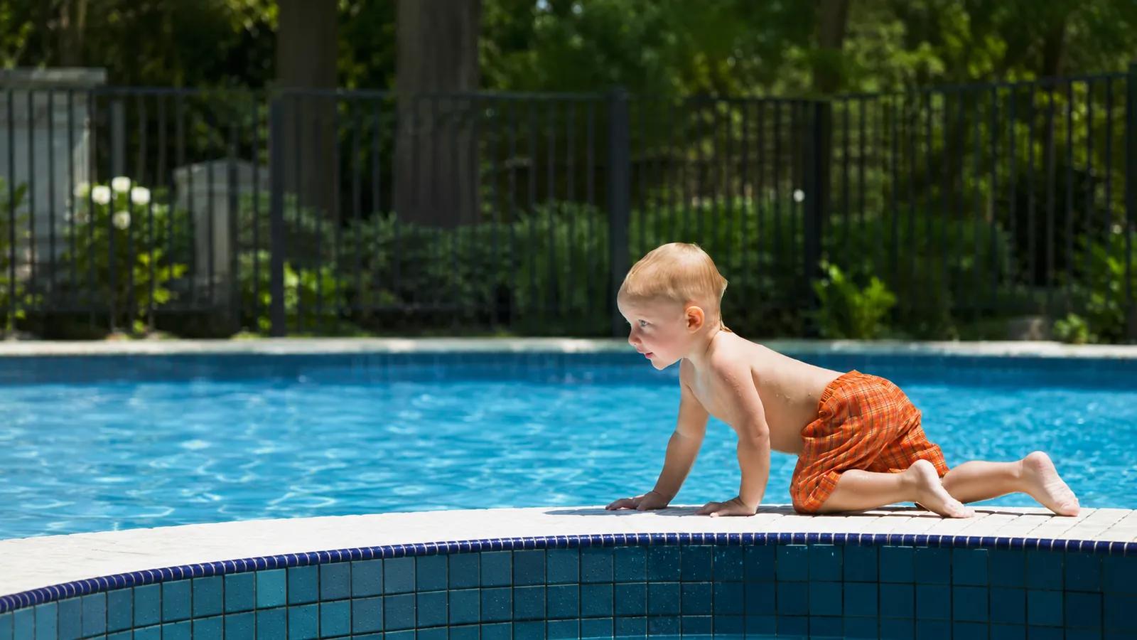 A young child crawling at the edge of a backyard swimming pool with a safety barrier behind — why pool and spa barrier inspections matter